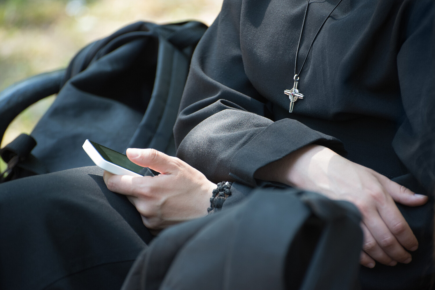 Unrecognizable nun in a black robe with a cross on his neck uses a smartphone Unrecognizable nun in a black robe with a cross on his neck uses a smartphone